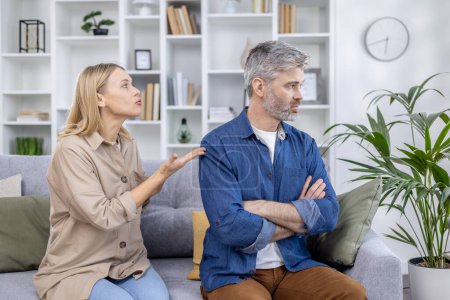 Un couple engagé dans une conversation sérieuse à la maison, avec la femme qui parle et l'homme qui regarde loin en silence.