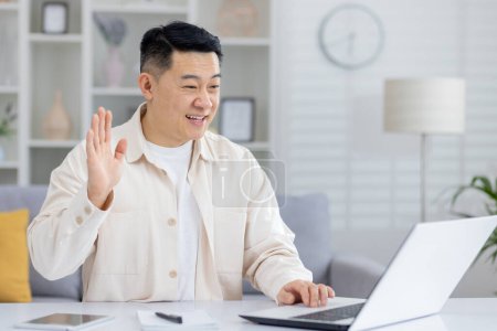 Un homme joyeux fait signe lors d'un appel vidéo depuis un bureau à domicile. Cadre décontracté et confortable, montrant l'utilisation de la technologie pour la communication.