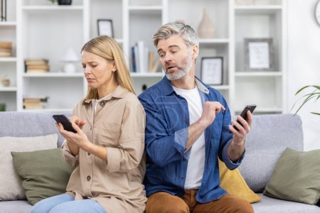 Couple sitting on couch looking upset while using smartphones, highlighting relationship issues and technologys impact on communication.