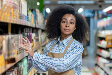 Employée d'un magasin portant un tablier organisant des produits sur une étagère de supermarché, présentant le travail de l'épicerie et la gestion de la vente au détail.