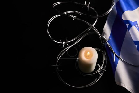 Foto de Flag of Israel, barbed wire and burning candle on black background. Holocaust memory day. - Imagen libre de derechos