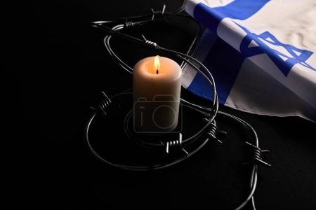 Flag of Israel, barbed wire and burning candle on black background. Holocaust memory day.