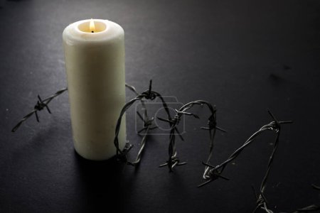 Holocaust-Gedenktag. Arbed Draht und brennende Kerze auf schwarzem Hintergrund.