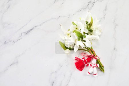 Photo for A bouquet of snowdrops flowers and a red-white martenitsa, a symbol of the holiday on March 1, Martisor, Baba Marta - Royalty Free Image