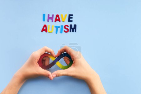 Autistische Jungenhände und Regenbogen-Acht-Unendlichkeitssymbol. Tag des Autismus-Bewusstseins