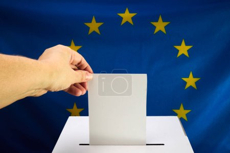 Hand placing a voting ballot into a clear box with EU flag backdrop.