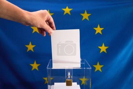 Déposer à la main un bulletin de vote dans une boîte avec le drapeau de l'UE en arrière-plan.