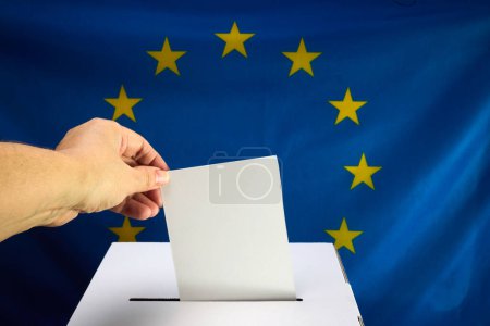 Hand wirft einen Stimmzettel in eine Schachtel mit EU-Flagge im Hintergrund.