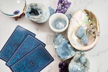 An assortment of gemstones, crystals, and tarot cards on a marble surface.