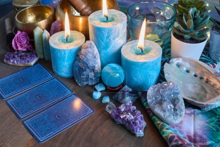 Eine Auswahl an Kerzen, Kristallen und Tarotkarten auf einer Holzoberfläche schafft eine mystische Atmosphäre.