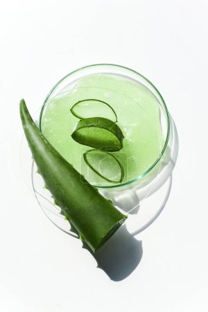 Top view of fresh aloe vera gel with slices and leaf on a white surface.