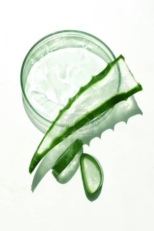 Pot en verre transparent rempli de gel d'aloe vera, entouré de feuilles d'aloe fraîches.