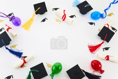 Top view of graduation caps, diplomas, and colorful balloons on white.