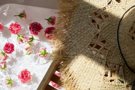 Eine ruhige Umgebung mit einem Strohhut neben einem Bad mit schwebenden rosa Rosen.