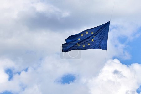 EU flag fluttering in the wind with a backdrop of a cloudy blue sky.