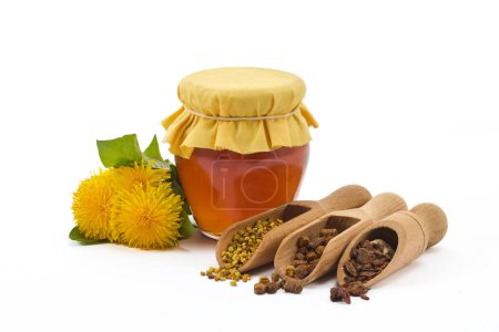Foto de Un frasco de miel con tapa de tela, gránulos de polen, pan de abeja y flores de diente de león. - Imagen libre de derechos
