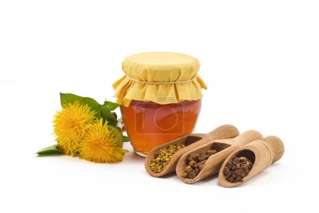 A jar of honey with fabric lid, pollen granules, beebread, and dandelion flowers.