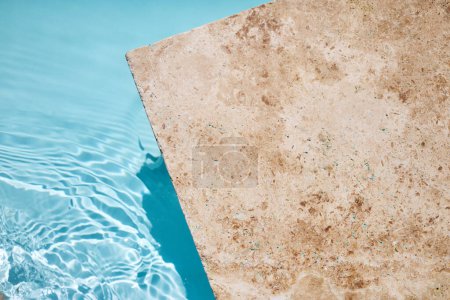 Un rincón sereno de una piscina con agua azul clara y una terraza con textura.