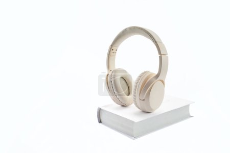 A pair of beige headphones resting on a white hardcover book against a white background.