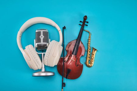 Un violín, saxofón, micrófono vintage y auriculares sobre un fondo azul.