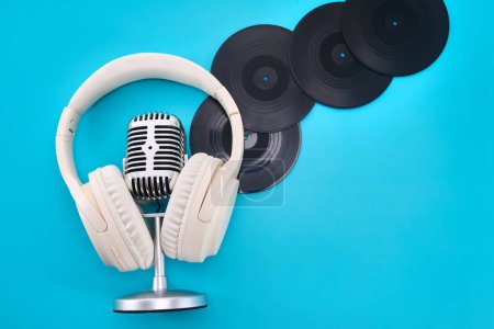 A vintage microphone, white headphones, and vinyl records on blue background.