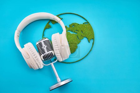 A top view of white headphones and a retro microphone on a green globe against a blue background.