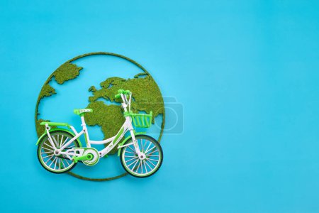 A green bicycle model on a moss-covered world map cutout against a blue background.