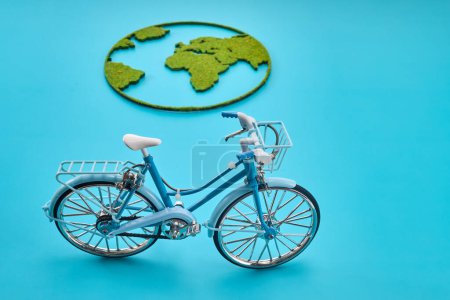 Un vélo miniature avec une carte du monde couverte d'herbe sur un fond bleu.