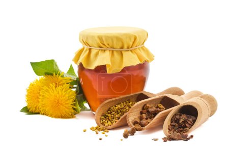 A jar of honey with fabric lid, pollen granules, beebread, and dandelion flowers.