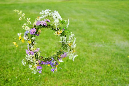 A vibrant floral wreath lies on lush green grass, featuring white, yellow, and purple flowers.