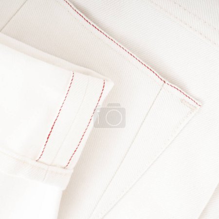 Detail of the bottom of milky raw denim jeans with red selvedge close up