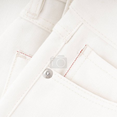 Pocket detail of milky raw denim jeans with red selvedge and metal fittings close up