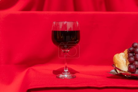 Foto de Copa de vino, pan y uvas sobre tela roja en luz dura. Simbolismo de la última cena de Cristo Jesús - Imagen libre de derechos