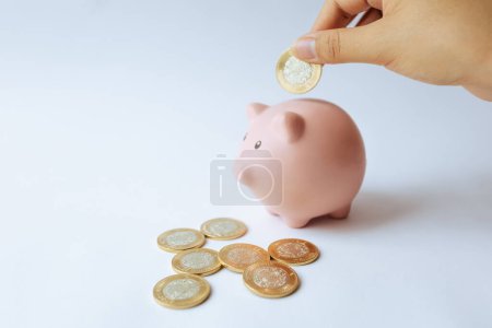 Una mano deposita una moneda en una figura de cerdo. Monedas de diez pesos mexicanos. Ahorro y economía en México