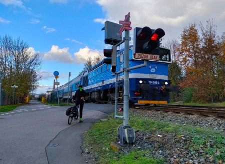 Prague, Czech Republic - November 5, 2022: A train is passing through railway crossing with stoplights being turned on. A cyclist is waiting for the train to go through.