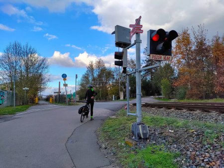 Foto de Un ciclista está esperando en el cruce ferroviario con semáforos encendidos. El clima es soleado.. - Imagen libre de derechos