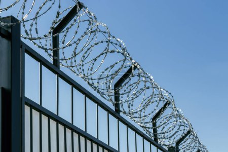 Téléchargez les photos : Barbed wire on an iron fence. Against the background of the blue sky. - en image libre de droit