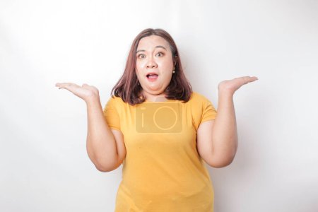 Photo for A portrait of an Asian big size woman wearing a yellow shirt shrugging her shoulder looks so confused, isolated by a white background - Royalty Free Image