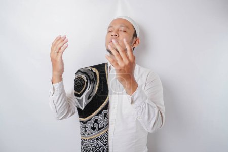 Photo for Happy handsome Asian Muslim man with prayer rug on his shoulder is praying to God. - Royalty Free Image