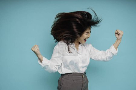 Téléchargez les photos : Une jeune femme asiatique avec une expression heureuse et réussie portant une chemise blanche isolée par un fond bleu - en image libre de droit