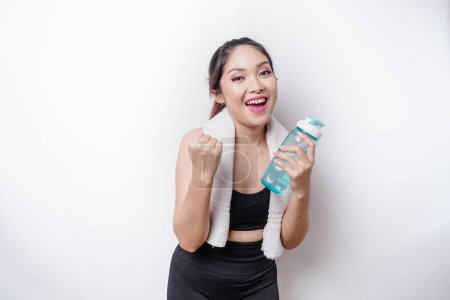 Photo for Smiling successful sportive Asian woman posing with a towel on her shoulder and holding a bottle of water - Royalty Free Image