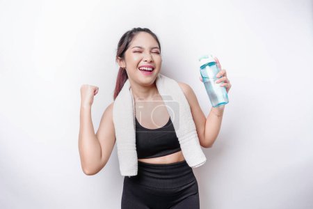 Photo for Smiling successful sportive Asian woman posing with a towel on her shoulder and holding a bottle of water - Royalty Free Image