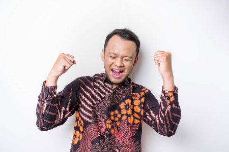 Photo for A young Asian man with a happy successful expression wearing batik shirt isolated by white background - Royalty Free Image