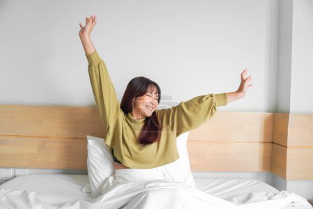 Téléchargez les photos : Portrait de beauté femme asiatique heureuse se réveillant, se réveiller sur le lit (sommeil). Jeune belle fille asiatique étirant ses bras en début de matinée fraîche, se détendre paisible matin routine bâillement concept bannière - en image libre de droit