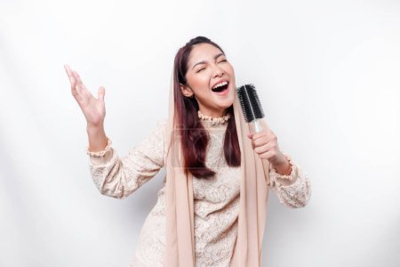 Téléchargez les photos : Portrait de femme musulmane asiatique insouciante, s'amusant karaoké, chantant au microphone tout en se tenant sur fond blanc - en image libre de droit
