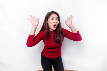 Photo for Shocked Asian woman dressed in red, pointing at the copy space above her, isolated by white background - Royalty Free Image
