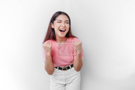 Eine junge Asiatin mit glücklichem, erfolgreichen Gesichtsausdruck trägt ein rosafarbenes T-Shirt vor weißem Hintergrund