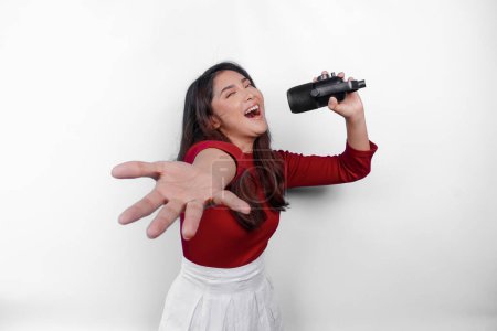 Portrait of carefree Asian woman, having fun karaoke, singing in microphone while standing over white background