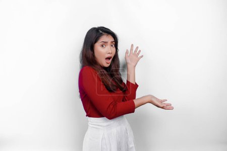 Photo for Shocked Asian woman wearing red t-shirt, pointing at the copy space on beside her, isolated by white background - Royalty Free Image