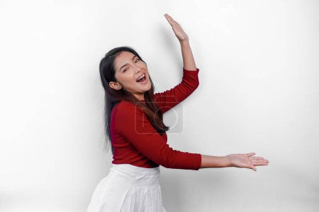 Aufgeregte Asiatin in rotem T-Shirt, die auf den Kopierraum neben ihr zeigt, abgeschirmt von weißem Hintergrund